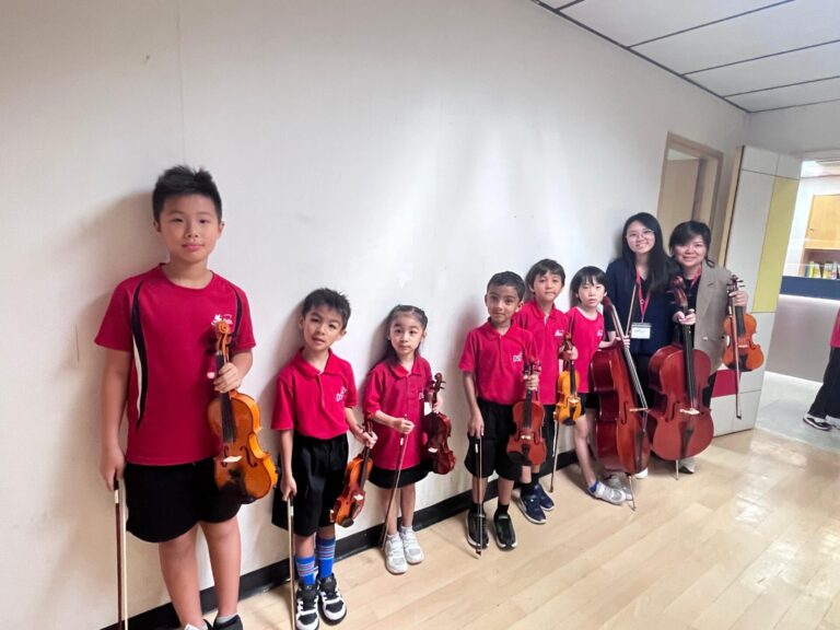 Group of young orchestra students with violins and a cello posing with their Sophie and Lorraine, showcasing the community at PURE.